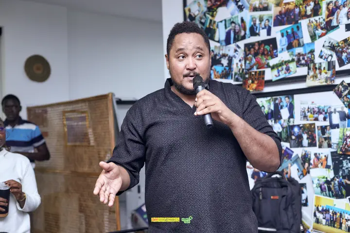 A meetup host speaking into a microphone in front of community photographs